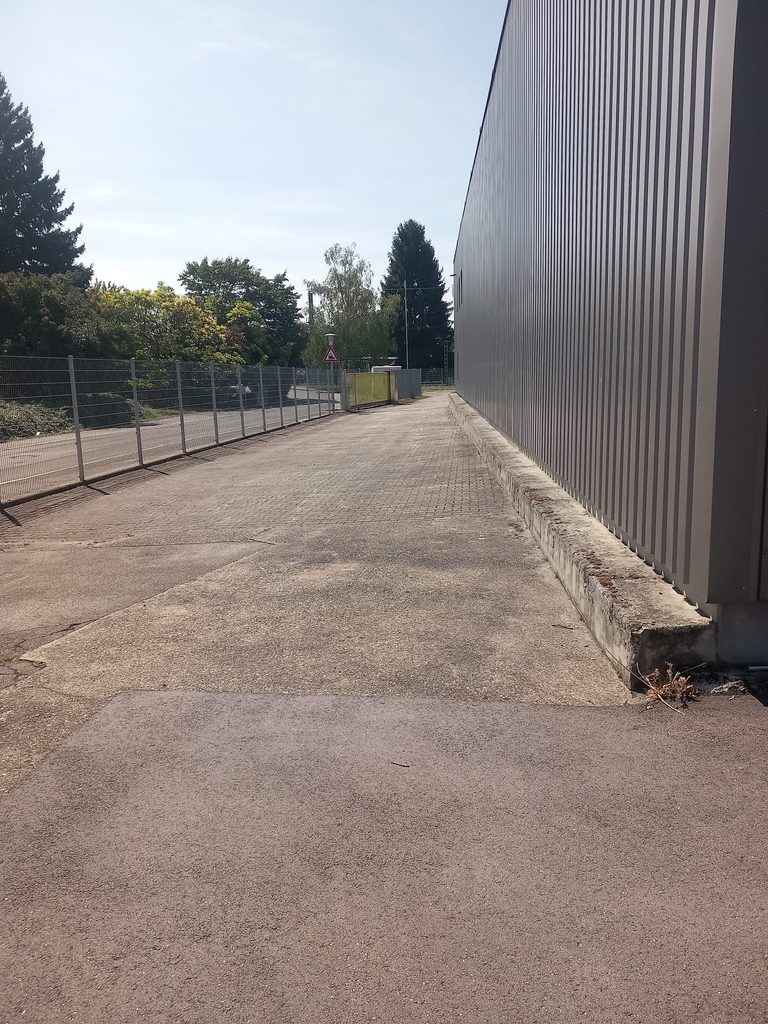 Gepflegter Weg entlang der Hallenwand mit Zaun, Außenreinigung bei Grammer