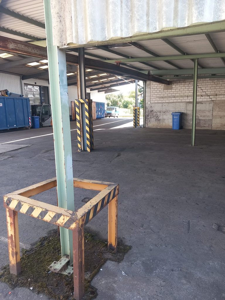 Gereinigter Unterstand mit gelb-schwarzer Schutzbarriere und Containerstellplatz bei Grammer